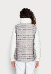 Chaleco acolchado blanco con un respaldo texturizado de tweed multicolor. Presenta un cuello alto, bolsillos laterales y un corte relajado.