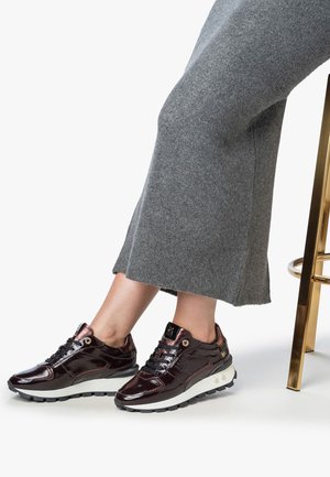 Sneakers in pelle verniciata color marrone scuro con suole nere, dotate di lacci scuri, accenti metallici e una gonna in lana grigia testurizzata.