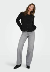 Cardigan noir à boutons, avec un ourlet froncé et des boutons à l'avant, associé à un jean ample gris et des bottines à talons carrés noires.