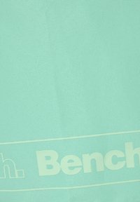 Svijetlo mint zelena tkanina glatke teksture, sa velikim bijelim "Bench." logotipom otisnutim duž dna. Jednostavan, čist dizajn.
