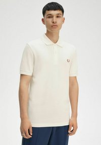 Polo shirt crema realizzata in tessuto testurizzato, con patta a due bottoni e logo ricamato sul lato sinistro del petto. Maniche corte.
