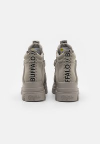 Kerged sneakerid heledes suedes, paksu kummitallaga, musta logoga ja triibulise tõmblukuga taga.