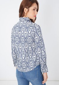 Camisa de manga larga con un patrón geométrico en azul y blanco, con cuello, detalles de botones y un corte relajado. Material de algodón.