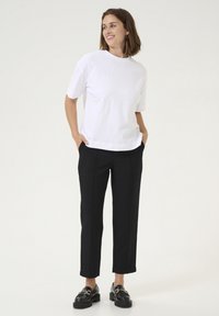 T-shirt bianco in cotone con vestibilità rilassata, abbinato a pantaloni neri a vita alta con gamba dritta e sottili pieghe frontali. Mocassini neri.
