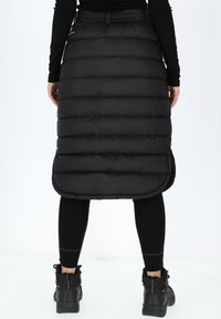 Black puffer skirt with horizontal quilted sections, knee-length, elastic waistband, and side slits, paired with black leggings and boots.