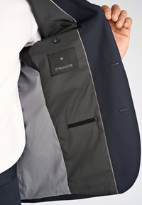 Granatowa marynarka z szarą podszewką, z metką oznaczoną "JUNK de LUXE" oraz ukrytą kieszenią. Widoczna faktura tkaniny.