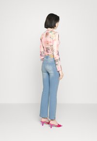 Top rosa transparente de mangas longas com estampas florais e gráficas, combinado com jeans de cintura alta azul claro e sandálias de salto rosa.
