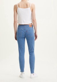 Světlé modré džíny skinny s středním pasem, dvěma zadními kapsami a koženou nášivkou se značkou. Bílý zkrácený top bez rukávů a tenisky.