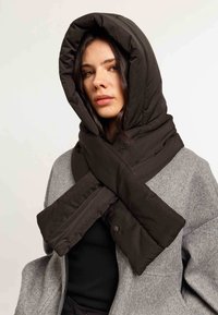 Scarf nera imbottita con un ampio cappuccio, avvolta a forma di X attorno al collo, abbinata a un cappotto grigio. Texture liscia, design trapuntato.