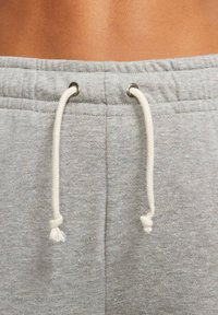 Šedé tepláky s hladkou texturou, vybavené stahovací šňůrkou s bílými konci, kovovými průchodkami a všitou gumou v pase.