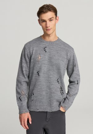 Maglione grigio a maglia con scollo rotondo, caratterizzato da dettagli sdruciti intenzionali e polsini e orlo a costine. Design sobrio e con una texture interessante.