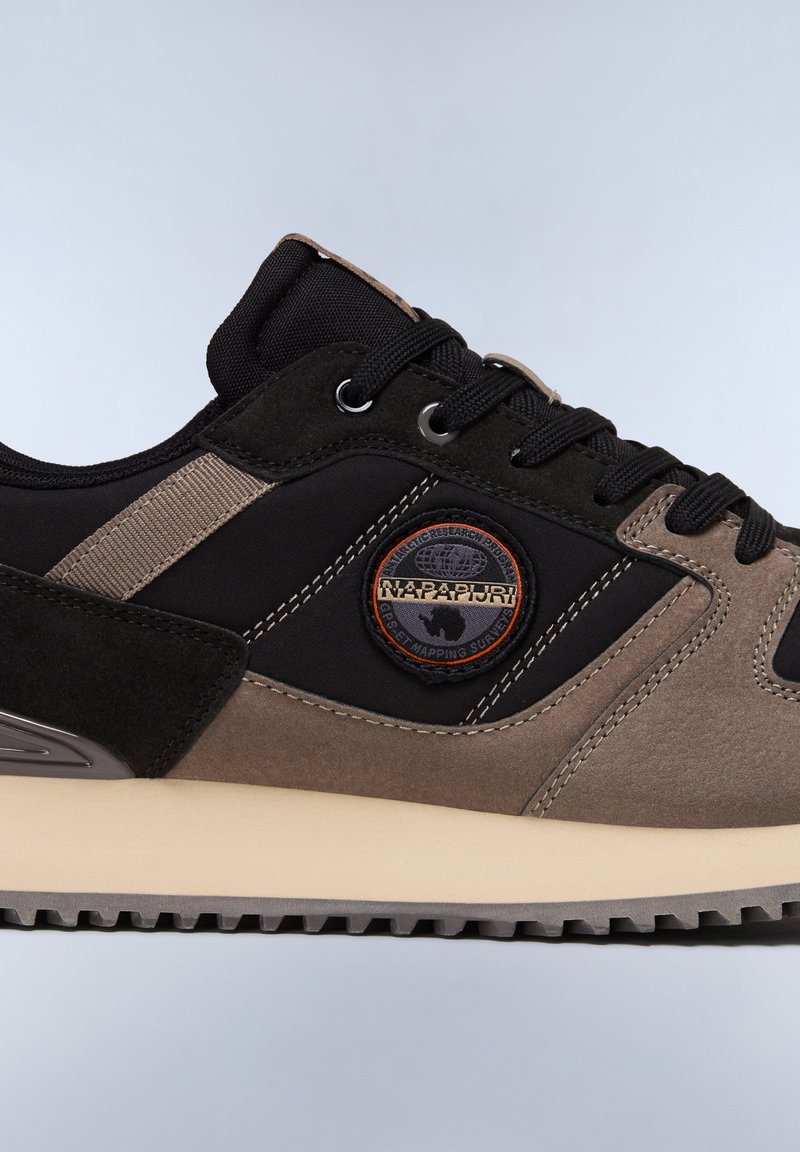 Zapatillas con parte superior de tela negra, detalles en ante gris y un logotipo circular. Cuentan con una media suela acolchada y una suela exterior de goma texturizada.