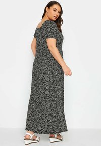 Maxi dress con maniche a palloncino corte, tessuto nero con motivo floreale bianco, corpino aderente e gonna fluida. Indossato con sandali con tacco a cuneo bianchi.