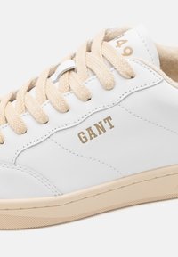 Weiße Leder-Sneaker mit beige Akzenten und strukturiertem Gummisohle. Verfügt über beige Schnürsenkel und das goldene "GANT"-Logo an der Seite.