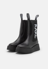 Black leather ankle boots featuring a chunky platform sole, elastic side panels, and logo accents on each heel tab. Smooth finish and rounded toe.