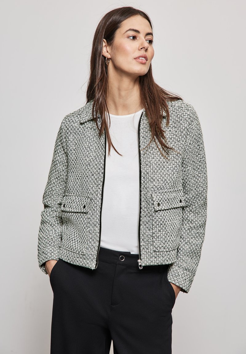 Textured jasje in een zwart-wit houndstooth patroon, met een rits aan de voorkant, twee voorkeurszakken en een kraag. G gedragen over een witte top.