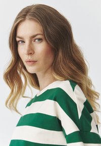Pull rayé vert et blanc avec un col rond, fabriqué en matériau doux, présentant une coupe décontractée et une texture subtile.