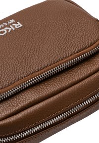 Portafoglio in pelle marrone con texture, dettagli in cerniera argentata e logo impresso sulla superficie. Design compatto con cuciture visibili.