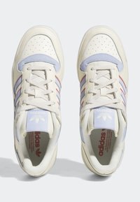 Zapatillas deportivas en crema y azul claro con puntera perforada, acentos rojos, cierre de cordones y cuello acolchado con el logo en la lengüeta.
