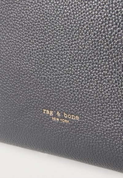 Μαύρη επιφάνεια από δέρμα με υφή πετρωμάτων και χρυσά γράμματα που σχηματίζουν τη φράση "rag & bone NEW YORK" κεντραρισμένη κοντά στον πάτο.