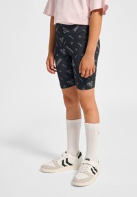 Svarta cykelshorts med vita logotyper, kombinerat med vita sneakers med svarta ränder och krämfärgade detaljer, kompletterat med knähöga vita strumpor.