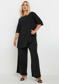 Completo black a due pezzi composto da un top largo e testurizzato con maniche ampie e fessure laterali, abbinato a pantaloni fluidi a gamba larga.