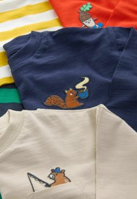 Kinderbekleidung mit gestickten Tiermotiven: ein Eichhörnchen mit einer dampfenden Tasse auf einem navyblauen Shirt und ein Bär beim Angeln auf einem beige Shirt.