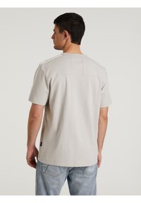 Camicetta grigia chiara a maniche corte con scollatura rotonda, caratterizzata da un dettaglio di cucitura sul retro e accenti a contrasto sulle spalle. Realizzata in cotone morbido.