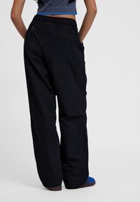 Zwarte, losse buitenbroek met een elastische tailleband en ritszakdetails. Gemoedelijke textuur en recht model.