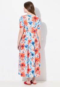 Robe maxi florale en tissu léger, présentant un imprimé coloré de fleurs rouges et bleues, des manches courtes bouffantes et une couture à la taille.