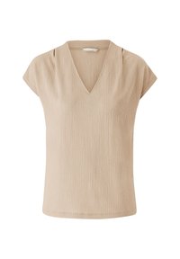 Haut beige à manches courtes avec un col en V, présentant un tissu texturé et un léger drapé aux épaules pour plus de détails.