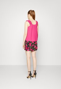 Top sem mangas fúcsia com alças em renda, combinado com uma saia mini preta com flores em rosa, usada com sandálias de salto alto pretas.
