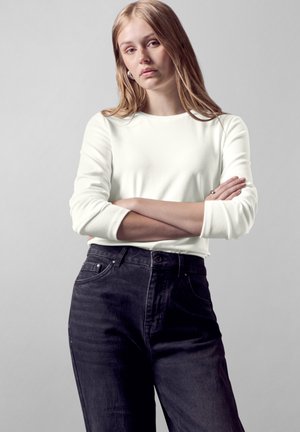 Witte lange mouwen top met een ronde hals, gecombineerd met donkere, aansluitende jeans. De stof lijkt glad te zijn, met een minimalistisch ontwerp.