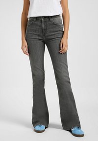 Jeans negros de corte acampanado, confeccionados en denim, con cintura alta, ajuste recto y textura desgastada. Combinados con zapatillas azules.