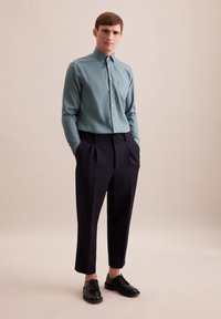 Lichtblauw longsleeve shirt met een puntige kraag en een borstzak, gecombineerd met hoge, donkerblauwe broeken en zwarte schoenen.