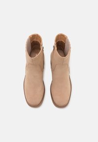 Stivaletti alla caviglia in suede beige con una finitura liscia, dotati di una cerniera laterale, punta arrotondata e cuciture a contrasto lungo la suola.