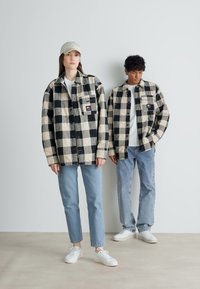 Juodi ir kreminiai langeliais raštuoti švarkai su dviem priekinėmis kišenėmis, dėvimi dviejų modelių. Jie vilki šviesiai mėlynas džinsus ir baltus sportinius batelius.