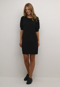 Robe noire à manches courtes avec une coupe ample et un col rond. Tissu lisse de couleur unie, assorti à des mocassins noirs.