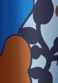 Gros plan sur un tissu bleu présentant un motif floral coloré avec des formes marron, noir et bleu clair. Texture lisse avec une finition mate.