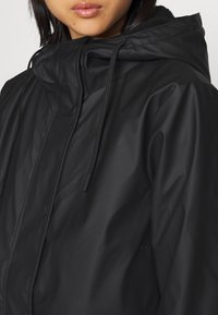 Schwarze wasserdichte Jacke mit hohem Kragen, verstellbaren Kordeln und glatter, glänzender Textur. Keine sichtbaren Muster oder Beschläge.