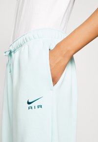 Světle modré tepláky s elastickým pasem, bočními kapsami a tmavě modrým logem Nike AIR. Měkká tkanina s hladkým povrchem.