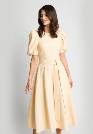 Sukienka z puff-sleeve, do kolan, w delikatnym żółtym materiale, z dopasowaną górą i wiązanym paskiem w talii. Zwiewna spódnica o gładkiej teksturze.