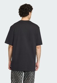 Čierne bavlnené tričko s krátkymi rukávmi, voľného strihu a hladkým chrbtom. Nosené so vzorovanými sivými šortkami s motívom listov.