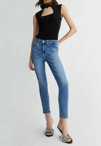 Černý bezramínkový top s výřezem a zdobením hřebíčky, zkombinovaný s úzkými modrými džíny a vzorovanými otevřenými sandály na podpatku.