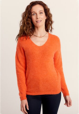 Sweater orange en V en matériau doux et moelleux avec des manches longues et des poignets côtelés, associé à un jean foncé.