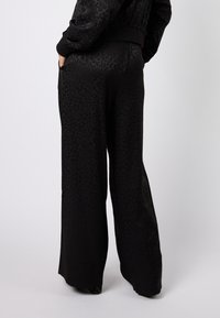 Czarne spodnie z szerokimi nogawkami o subtelnym wzorze w panterkę, z wysokim stanem i bocznymi kieszeniami. Materiał ma gładką fakturę.
