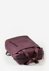 Zaino bordeaux con patta pieghevole, tasca esterna con zip e dettagli in pelle. Realizzato in materiale liscio e impermeabile con spallacci regolabili.