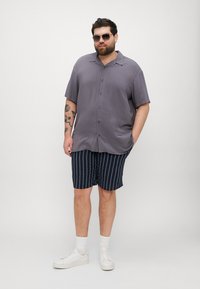 Kortermet, lys grå skjorte med knapper kombinert med marineblå stripete shorts. Hvite sneakers og sokker gir et avslappet preg.