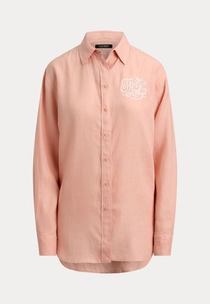 Pikad varrukad, nööpidega lahtikäiv virsikuvärvi särk terava kraega ja parema rinna kohal valgete tikitud initsiaalidega.