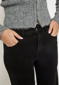 Crne traperice s uskim krojem, visokim strukom i prednjim džepovima. Uparen s sivim pletivom koje ima teksturirani uzorak.